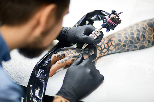 Modern tattooer painting on his client arm