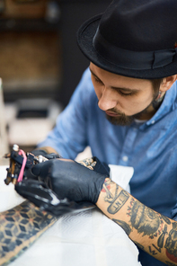 Concentrated tattooist painting adornment on client arm