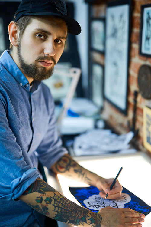 Bearded man in ball-cap making sketch of creative tattoo