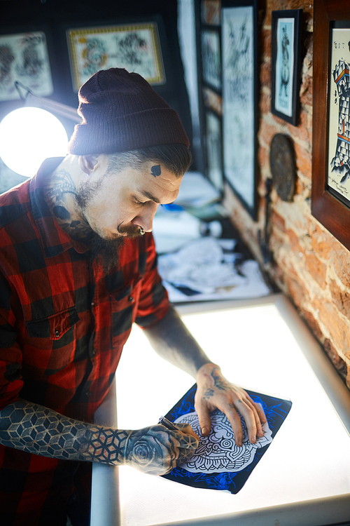 Creative man in tattoo workshop drawing adornment