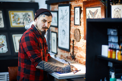 Young man making sample tattoo sketches in workshop
