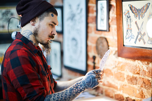 Hipster with tattooes looking at picture of drawn ornament