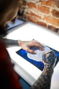 Hands of man with tattooes drawing ornament with pen