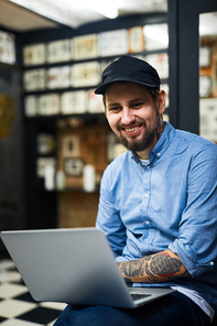 Happy tattooist with laptop working in the net