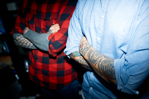 Two guys in shirts crossing their arms with tattooes on chest