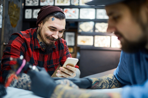 Happy hipster with smartphone visiting tattooist