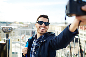Smiling traveler with camera making photo of himself