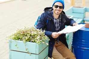 Tourist with map sitting on bench in urban environment