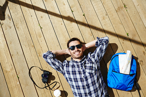 Restful tourist lying on wooden pontoon on sunny day