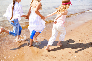 Group of little girls running down sandy beach on summer vacation