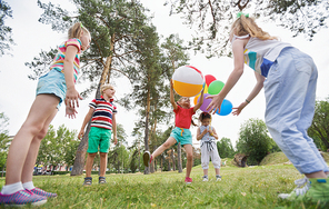 Low angle view of kids playing with beach ball in park while their little female friend standing behind with colorful balloons