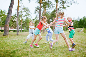 Group of children holding hands and dancing in circle on green lawn in park on beautiful summer day