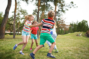 Group of happy kids holding hands and dancing together in circle in public park on warm summer day