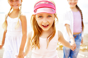 Laughing girl holding by hands of her friends and having fun on the beach