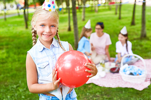 Pretty little girl playing with red balloon on background of her friends in park