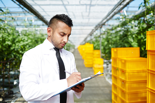 Young agro-engineer making notes on background of all year round vegetation