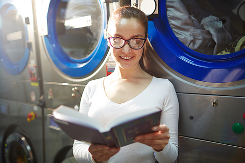 Pretty young woman reading in laundry