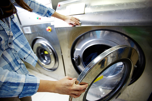 Woman closing porthole of automatic washing-machine