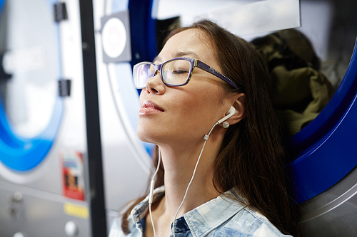 Girl in eyeglasses enjoying music while waiting for clean clothes