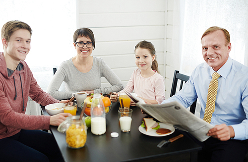 Lovely family of four  with wide smiles while having healthy breakfast at home, waist-up portrait