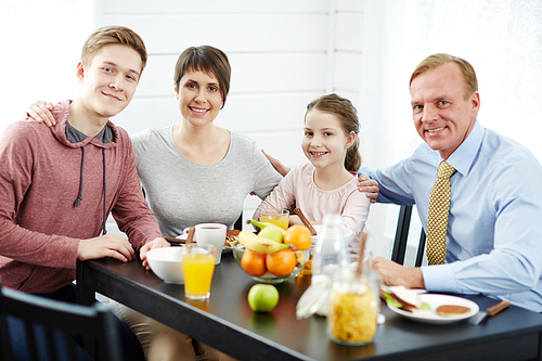 Cheerful parents and kids sitting by table in the kitchen