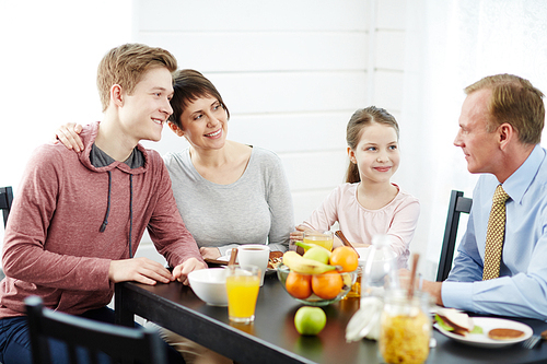 Close-knit family gathered together in kitchen, talking to each other animatedly and eating healthy breakfast, waist-up portrait