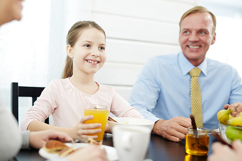 Smiling girl and her father sitting by table by breakfast