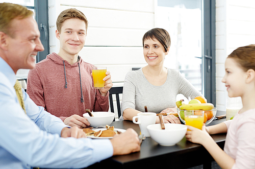 Joyful family members gathered together in dining room, enjoying tasty breakfast and chatting animatedly, waist-up portrait