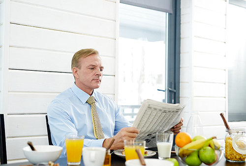 Businessman sitting by table with organic food and reading news