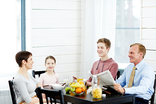 Cheerful modern family of four enjoying each others company while sitting in kitchen and eating healthy breakfast, waist-up portrait