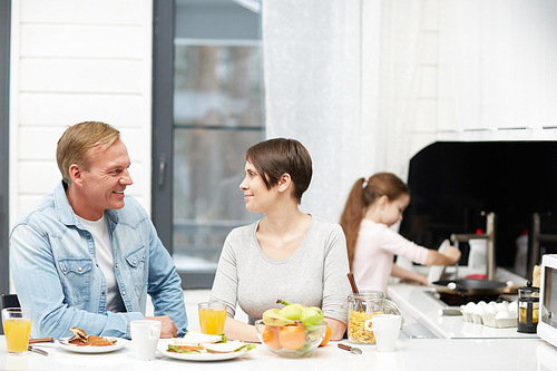 Happy couple interacting by breakfast in the kitchen with their daughter on background