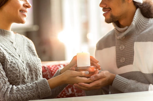 Young couple in sweaters holding burning candle on Christmas evening