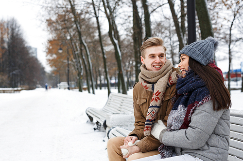 Young couple sitting on bench in park and having talk