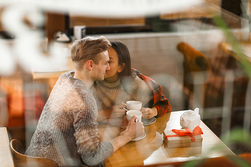 Amorous girl kissing her boyfriend on cheek while having tea in cafe
