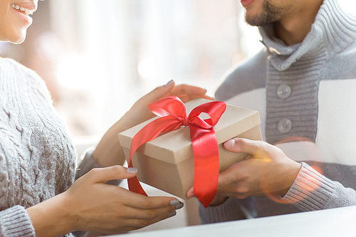Hands of young man giving xmas surprise in box with red ribbon to his girlfriend