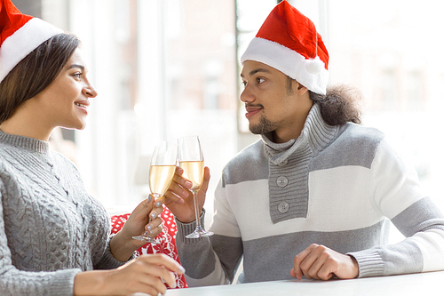 Young dates in Santa caps clinking flutes with champagne during celebration
