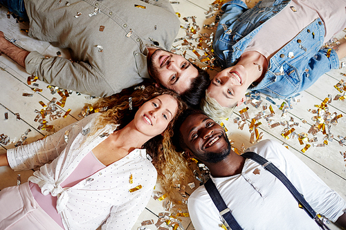 Four intercultural friends lying head to head on the floor covered with confetti