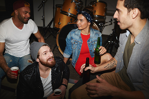 Group of trendy young people, men and woman, hanging out in night club, sitting on stage and drinking beer