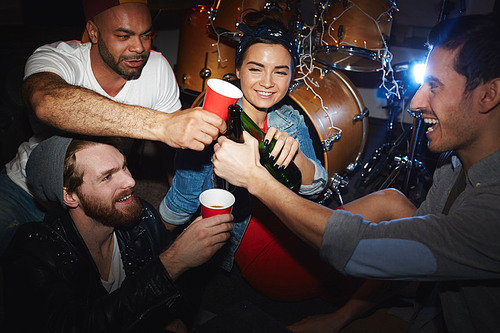Group of smiling young party people, men and woman,  drinking beer and raising glasses hanging out in night club