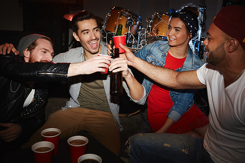 Group of smiling young party people drinking beer and raising glasses hanging out in night club on stage