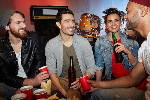 Group of smiling young people enjoying party in underground night club and drinking beer sitting on stage