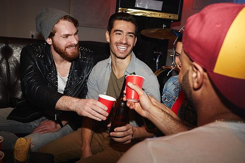 Group of smiling young people raising beer glasses hanging out at party and having fun