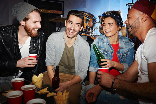 Happy guys and girl having beer with chips while talking at party in night-club