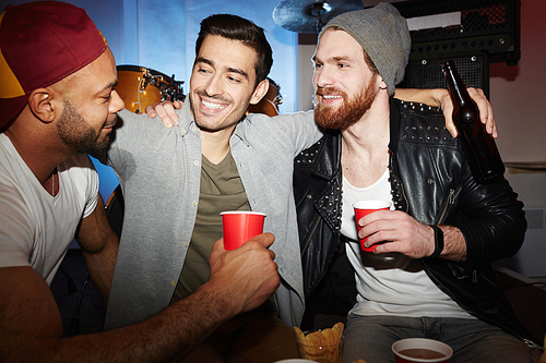 Three smiling young  men enjoying party in club, drinking beer and chatting