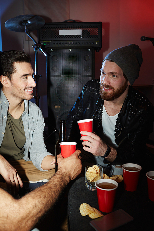 Trendy young men hanging out at late night party in dark club, drinking beer and chatting