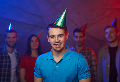 Happy guy in birthday cap and his friends on background