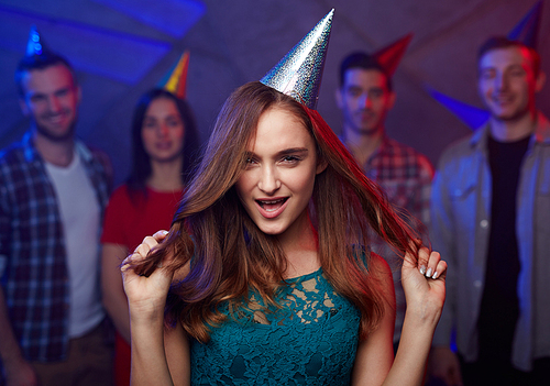 Girl in birthday cap holding ends of her long hair with flirty look
