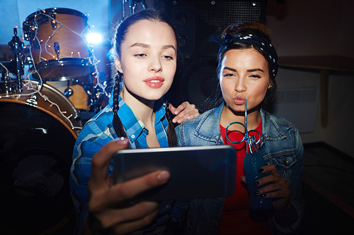 Portrait of two trendy teenage girls taking selfie in club, posing seductively