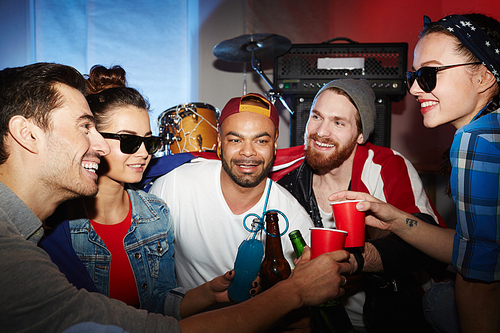 Multi -ethnic group of smiling young people hanging out in nightclub partying and toasting with beer, having fun