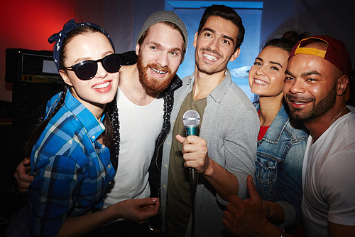 Multi-ethnic group of smiling young people hanging out in nightclub partying and having fun, singing karaoke on stage